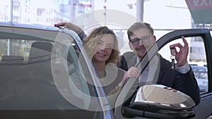 Auto buying, happy couple in love vehicle owners delight purchase and show keys in car sales center