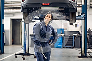 Auto car repair service center. Happy female mechanic standing by the car