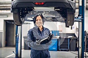 Auto car repair service center. Happy female mechanic standing by the car