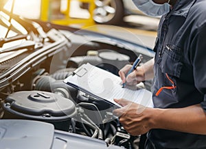 Auto check, car service shop concept. Automobile repairman writing job checklist on clipboard, mechanic checking engine