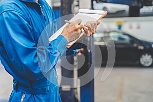 Auto check up and car service shop . Mechanic writing job checklist to clipboard to estimate repair quotation to client at