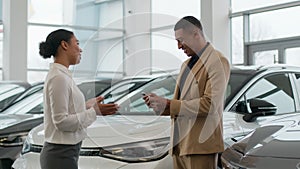 Auto dealer seller manager woman giving car key to happy owner African American man in dealership center successful sale