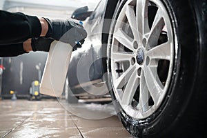 Auto detailing worker applies chemistry to wheels. Professional car wheel wash.