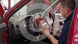 Auto electrician uses OBD2 diagnostic scanner to check vehicle fault codes on tablet in workshop. Car maintenance