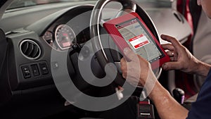 Auto electrician uses OBD2 scanner and tablet to diagnose vehicle faults. Professional mechanic checks car diagnostics