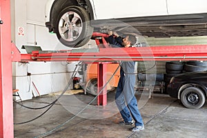 Auto Expert Repairing Car On Hydraulic Lift In Garage