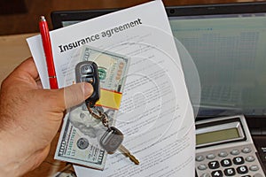 Auto insurance claim form with fountain hand, pen, car keys, much dollars, Laptop and calculator on the table