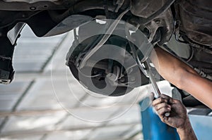 Auto mechanic asian checking bush-bolt under double wishbone suspension by hand with tools car lift