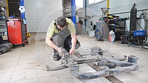 Auto mechanic assembles the subframe of car before installation at garage. Professional bearded repairman with special