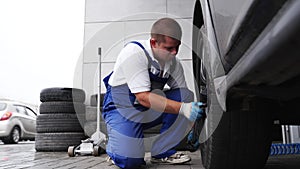Auto mechanic in blue uniform mounts tire using pneumatic wrench. Professional tire fitting, garage workflow. Skilled