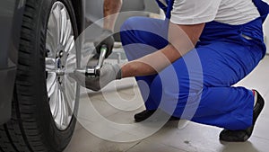 Auto mechanic in blue uniform tightens cars alloy wheel with torque wrench at modern auto repair shop. Skilled