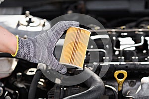 Auto mechanic changes oil filter for diesel cars, holds new oil filter in his hands against background engine
