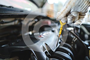 Auto mechanic is checking the oil in the vehicle in the car repair shop. He is wearing white gloves