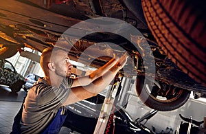 Auto mechanic checking running gear of automobile on service station. Male worker fixing problem with car. Vehicle maintenance