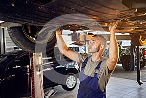 Auto mechanic checking running gear of automobile on service station. Male worker fixing problem with car. Vehicle maintenance