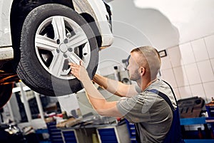 Auto mechanic checking running gear of automobile on service station. Male worker fixing problem with car. Vehicle maintenance