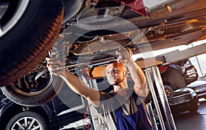 Auto mechanic checking running gear of automobile on service station. Male worker fixing problem with car. Vehicle maintenance