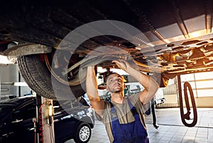 Auto mechanic checking running gear of automobile on service station. Male worker fixing problem with car. Vehicle maintenance