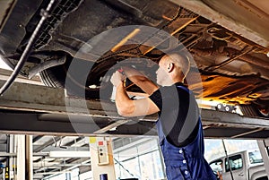 Auto mechanic checking running gear of automobile on service station. Male worker fixing problem with car. Vehicle maintenance