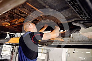 Auto mechanic checking running gear of automobile on service station. Male worker fixing problem with car. Vehicle maintenance