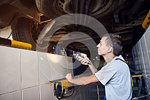 Auto mechanic checking running gear of automobile on service station. Male worker fixing problem with car. Vehicle maintenance