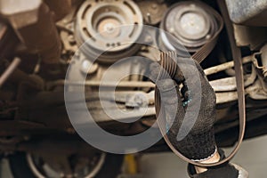 An auto mechanic checks the condition of the alternator belt for various defects by holding it in his hand