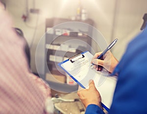 Auto mechanic with clipboard and man at car shop