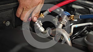 Auto mechanic connects hoses for car AC recharge service. Professional HVAC tech tools used for cooling system