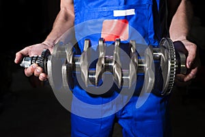 Auto mechanic with a crankshaft in his hands on a dark background. Repair service