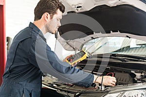 Auto Mechanic With Digital Multimeter Testing Car Battery