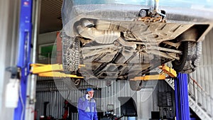 Auto mechanic discussing with customer on mobile phone under lifted automobile