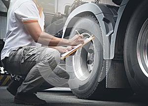 Auto Mechanic Driver Holding Clipboard is Checking A Truck Wheels and Tires. Inspection Maintenance and Safety of Semi Truck.