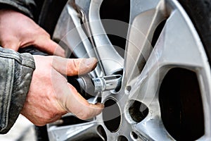 Auto mechanic with electric screwdriver changing tires on wheels outside.