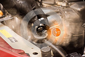Auto mechanic hand opens the radiator cap with steam escaping around the engine compartment,water temp gauge symbol.