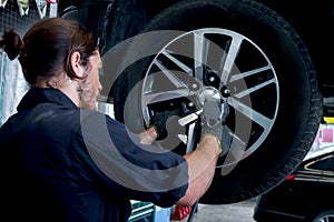 Auto mechanic handsome worker man checking wheel tires at garage, car service technician checking and repairing customer car at