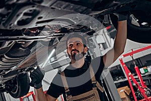 Auto mechanic in his workshop looking under a car on a hoist