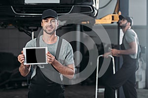 auto mechanic holding digital tablet with blank screen while colleague working