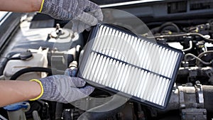 Auto mechanic holds car air filter in his hands near engine compartment, close-up. Concept of replacing auto parts