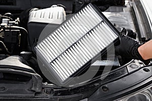 Auto mechanic holds car air filter in his hands near engine compartment, close-up. Concept of replacing auto parts