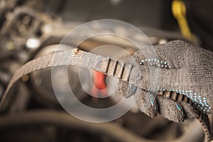 An auto mechanic holds in his hand a torn timing belt with worn out teeth against the background of a car engine