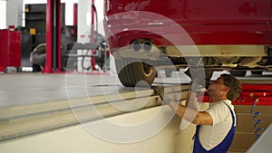 Auto mechanic inspects car steering, suspension at service station. Uses hydraulic play detector for vehicle diagnostics