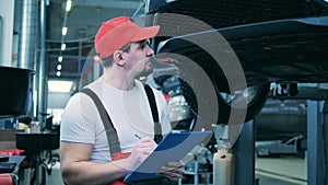 Auto mechanic inspects the underside of a car and takes notes. Auto mechanic working at car service.