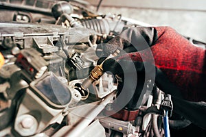 A auto mechanic is installing automobile iridium spark plugs into the ignition socket of the engine block