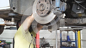 Auto mechanic installing part to car at garage or service. Professional repairman working underneath a lifting vehicle