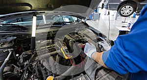 Auto mechanic man with multimeter testing battery