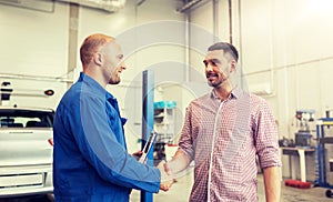 Auto mechanic and man shaking hands at car shop