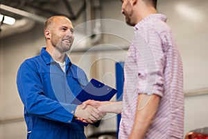 Auto mechanic and man shaking hands at car shop