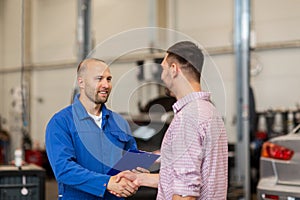 Auto mechanic and man shaking hands at car shop