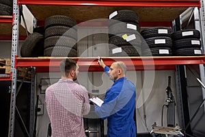 Auto mechanic and man with tires at car shop