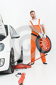 auto mechanic in orange uniform carrying car tire